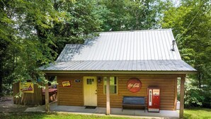 Een klein houten gebouw met een metalen dak, een Coca-Cola automaat en een bankje buiten.