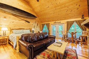 A cozy log cabin interior with a leather sofa, a wooden coffee table, and a dining area. - A Little River Romance | Private Dock + Hot Tub (Mentone)