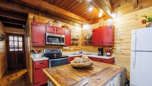 A cozy kitchen with wooden walls, red cabinets, a stainless steel microwave, a stove, and a white refrigerator.