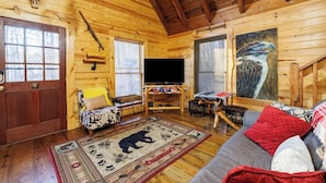 A cozy cabin interior with wooden walls, a bear rug, a television, and a painting of a bird.