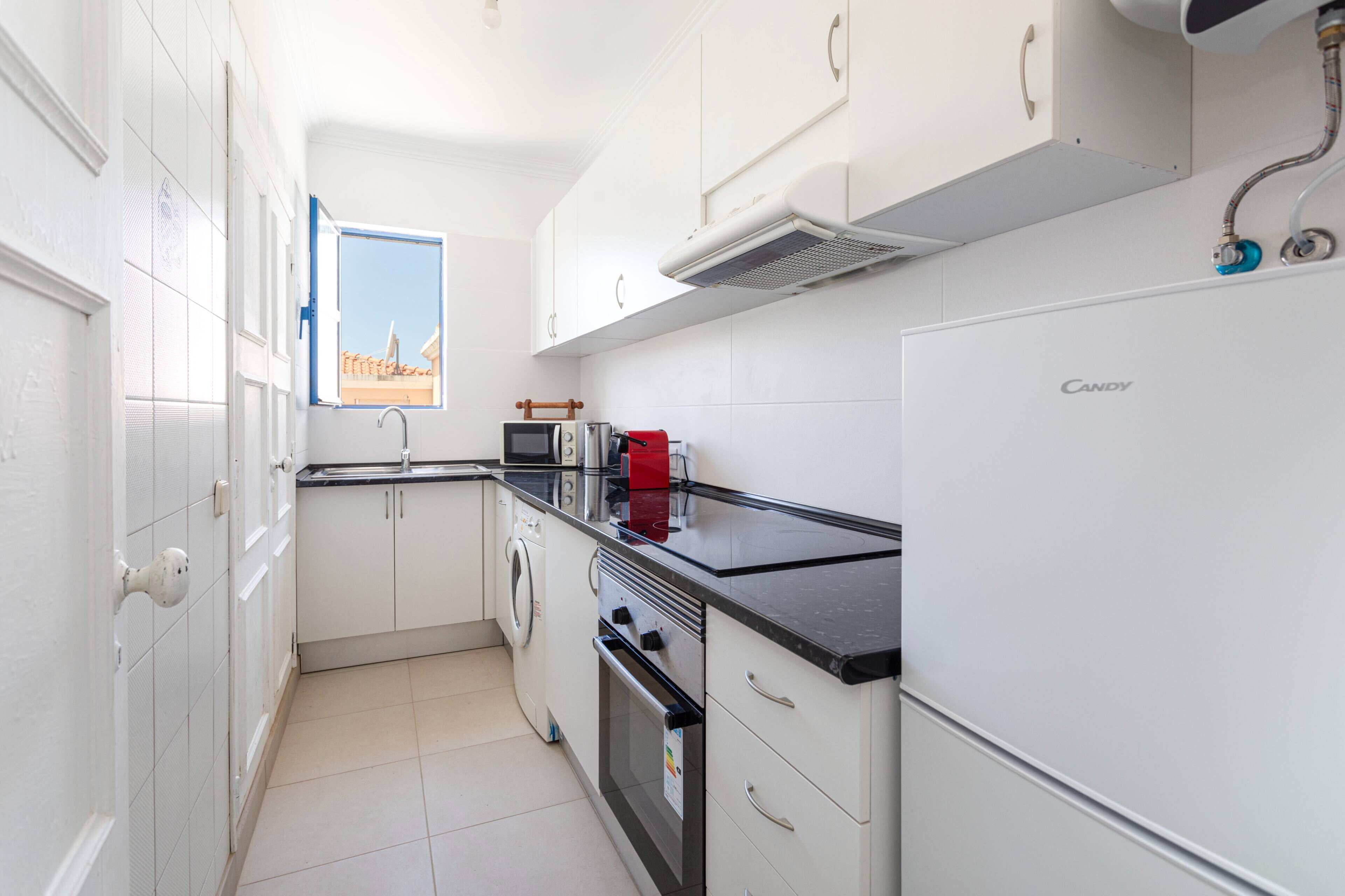 Una cocina compacta con armarios blancos, encimera negra, horno empotrado, microondas y refrigerador.