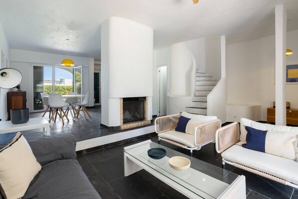 A modern living room with a fireplace, white sofas, and a glass coffee table.