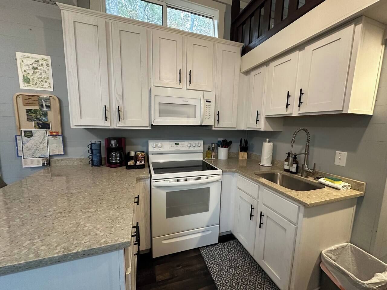A kitchen with white cabinets, a double oven, a sink, and a granite countertop.