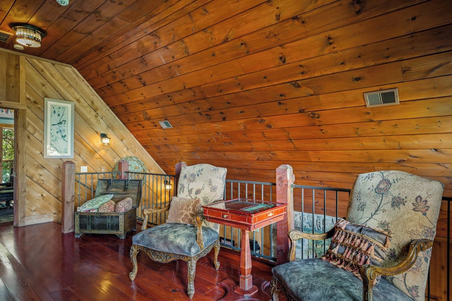 Ein Holzkaminzimmer mit schrägen Wänden, einem kleinen Tisch und zwei gepolsterten Stühlen mit Blumenmuster.