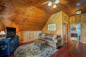 A cozy cabin interior with a wooden ceiling, a television on a dresser, a sofa with cushions, and a patterned rug. - Paradise Found - Lookout Mt Edge, Hot Tub & Views (Mentone)