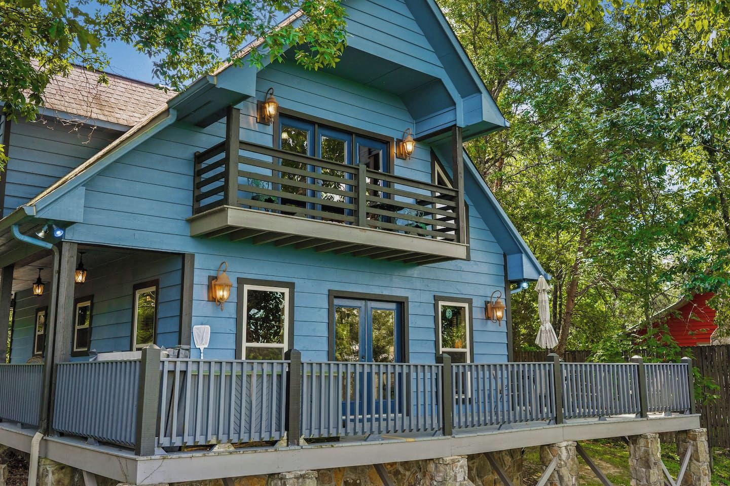 Une maison à deux étages avec un balcon, une terrasse en bois et, au fond, une construction dont le toit est rouge.