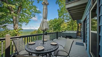 A deck with a round table and chairs, a covered umbrella, and a hot tub.