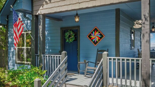 A blue house with a porch, a welcome sign, and a colorful geometric decoration.