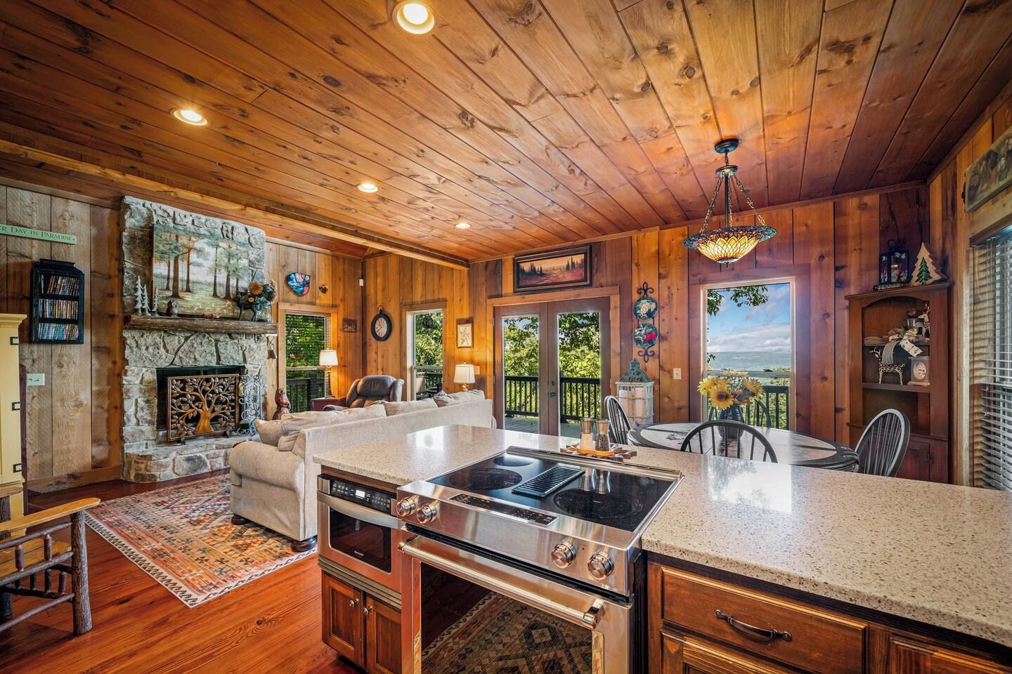 Un intérieur de chalet chaleureux avec une cheminée en pierre, un coin repas et une cuisine équipée d’une cuisinière intégrée.