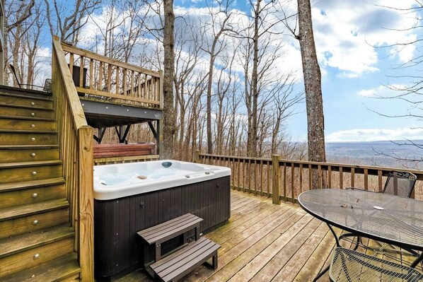 A wooden deck with a hot tub, a table, and benches.