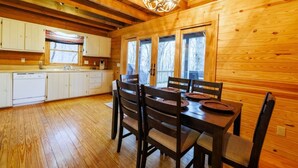 A wooden cabin interior with a dining area, kitchen, and large windows. - Serene Getaway | Hot Tub & Mountain Views (Mentone)