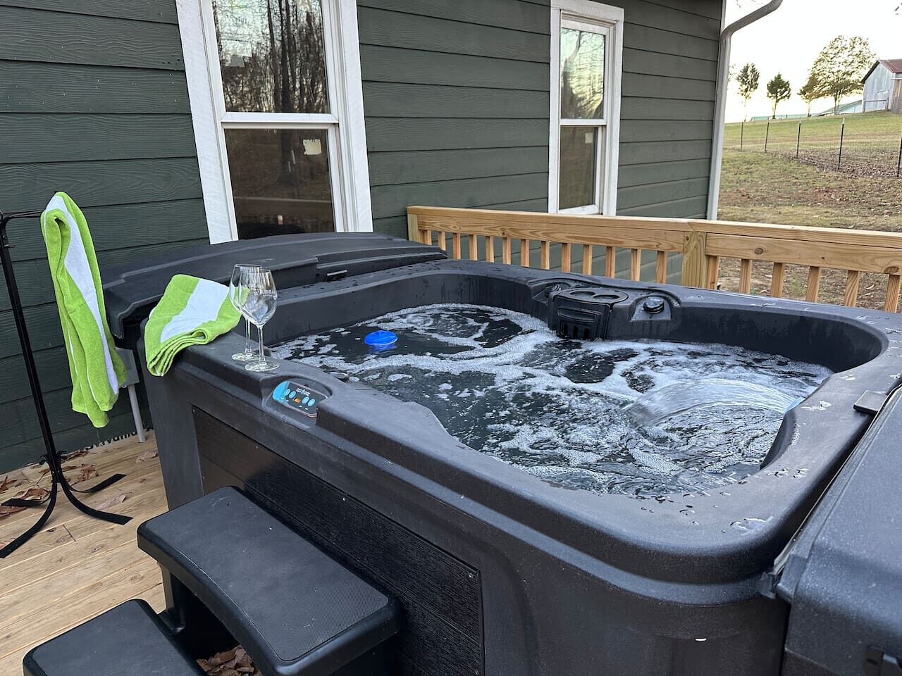 A hot tub with a control panel, a glass, and a towel on a wooden deck.