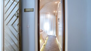 A hallway leading to a bedroom with a bed, a sign, and a door with a keyhole.