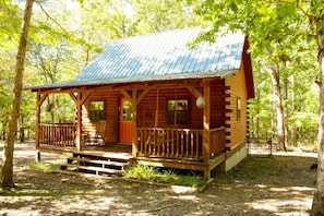 A rustic cabin with a porch, wooden deck, and a metal roof.