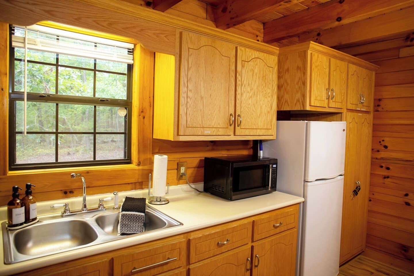 Une cuisine rustique aménagée dans une cabane en bois, avec un évier, un four à micro-ondes, un réfrigérateur et des placards en bois.