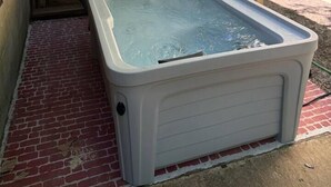 A hot tub in a covered outdoor area with a wooden deck and a brick floor.