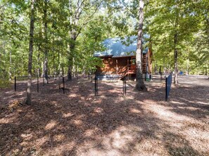 A cabin surrounded by trees with a metal fence in front. - Cabin in the Woods | Hot Tub, Fire Pit, BBQ (Mentone)