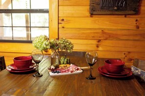 A wooden table with red plates, wine glasses, a vase with flowers, and a fruit platter. - Cabin in the Woods | Hot Tub, Fire Pit, BBQ (Mentone)