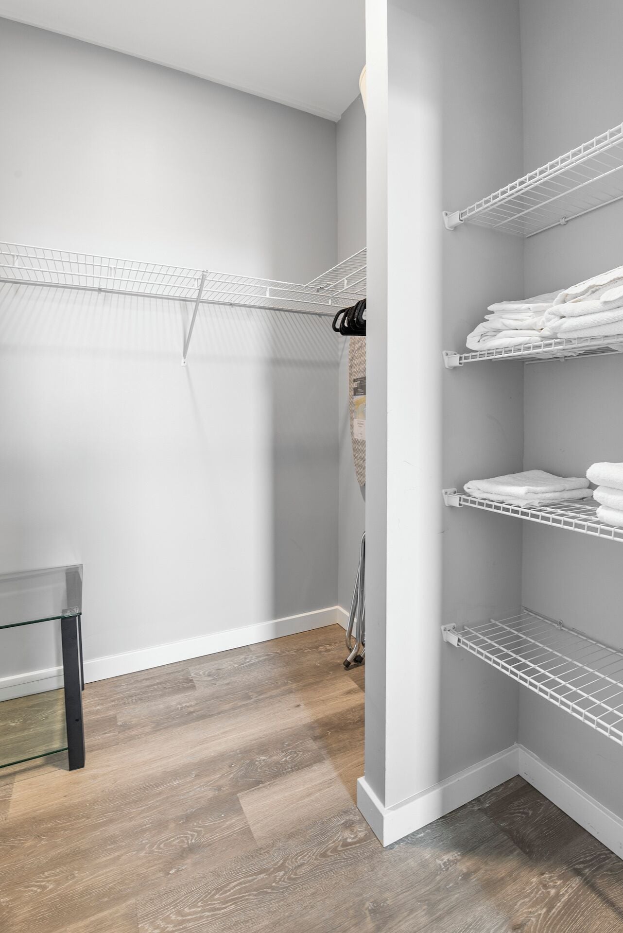 A walk-in closet with white shelving units and a metal drying rack.