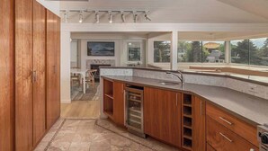 A modern kitchen with wooden cabinets, a built-in oven, and a large window offering a view of the outdoors. - Crow's Nest Condo 3BR Downtown (Anchorage)