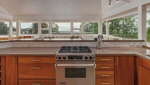 A modern kitchen with a built-in gas stove, wooden cabinets, and large windows offering a view of the outdoors. - Crow's Nest Condo 3BR Downtown (Anchorage)