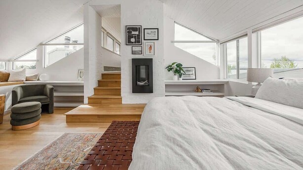 A modern loft bedroom with a large bed, a fireplace, and a staircase leading to an upper level. - Crow's Nest Condo 3BR Downtown (Anchorage)