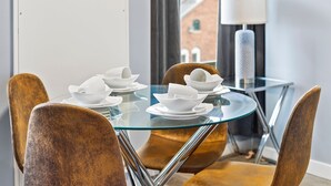 A dining area with a glass table, four chairs, and white bowls on plates. - Beautiful 1BR Near Encore Boston p273 (Everett)