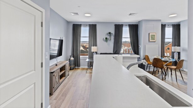 A modern kitchen with a central island, a dining area with chairs, a TV mounted on the wall, and a window with curtains. - Beautiful 1BR Near Encore Boston p273 (Everett)