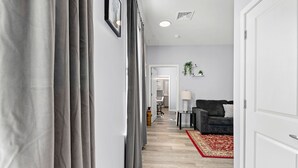 A hallway with grey curtains, a red patterned rug, a grey sofa, and a small table with a lamp. - Nice 1BR Near Encore Boston tl51 (Everett)