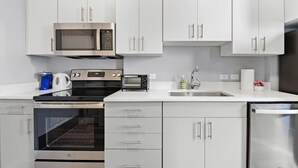 A modern kitchen with white cabinets, stainless steel appliances, a built-in oven, microwave, toaster, and a dishwasher. - Nice 1BR Near Encore Boston tl51 (Everett)