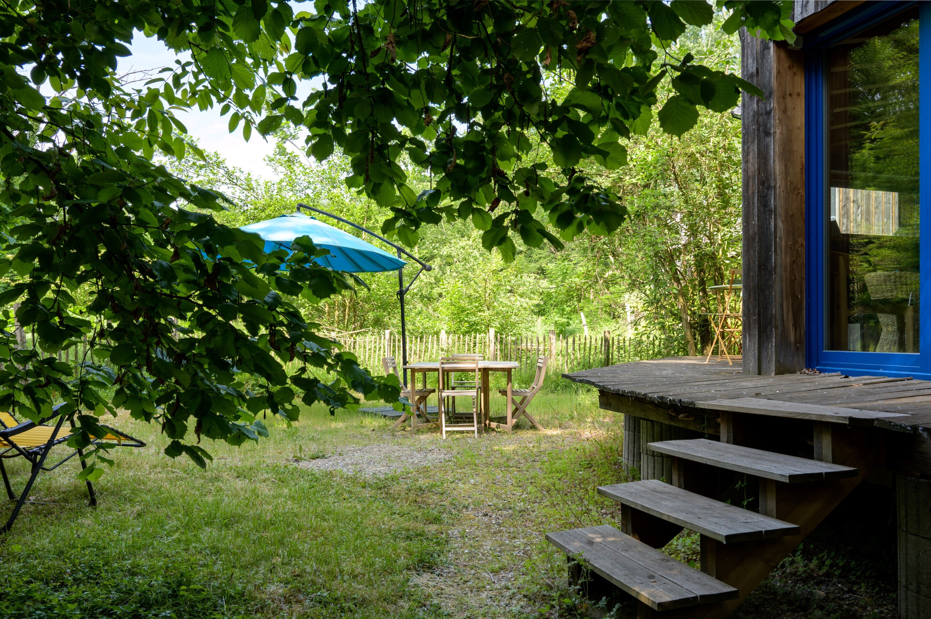 A wooden deck with a table and chairs, surrounded by a wooden fence and trees.