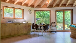 Una cocina con armarios de madera, una mesa de comedor con sillas, un reloj en la pared y puertas correderas de vidrio que dan a un jardín.