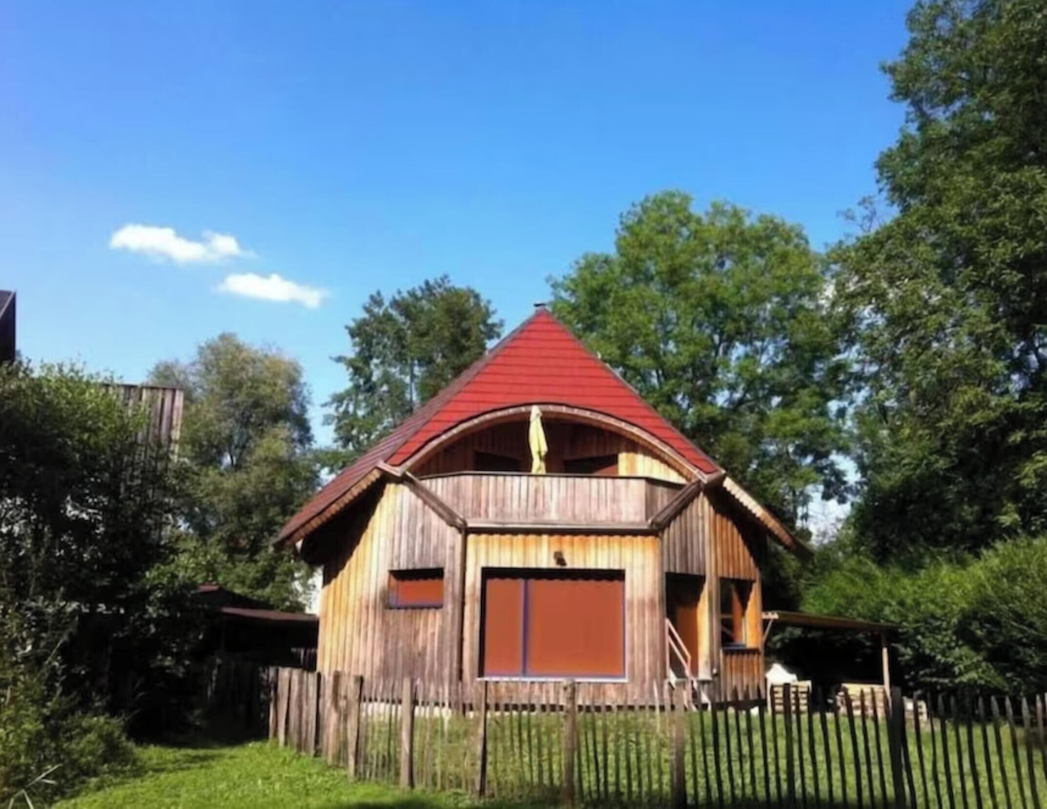 Una casa de madera con techo rojo, rodeada de árboles y una valla de madera.