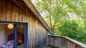 Una cabaña de madera con balcón, una cama con ropa de cama floral y vistas a los árboles.