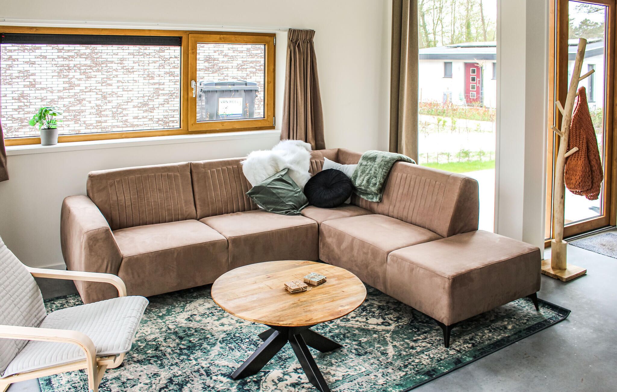 Ein modernes Wohnzimmer mit einem braunen Ecksofa, einem runden Couchtisch aus Holz und einem gemusterten Teppich.