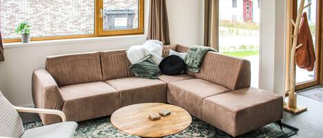 Ein modernes Wohnzimmer mit einem braunen Ecksofa, einem runden Couchtisch aus Holz und einem gemusterten Teppich.