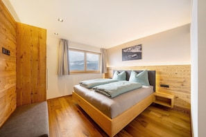 A bedroom with a wooden bed, a nightstand, a window, and a view of the outdoors. - Apartment 'Loach' with Mountain View, Shared Garden and Wi-Fi (Val d'Ultimo)