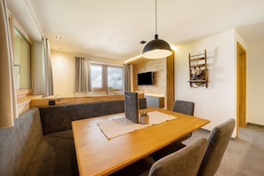 A modern dining area with a wooden table, grey upholstered chairs, a black pendant light, and a TV mounted on a wooden wall. - Apartment 'Loach' with Mountain View, Shared Garden and Wi-Fi (Val d'Ultimo)