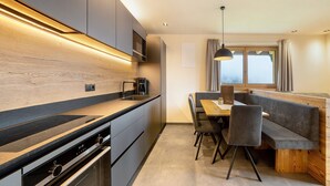 Una cocina moderna con electrodomésticos integrados, un comedor con banco y un ventanal con cortinas.