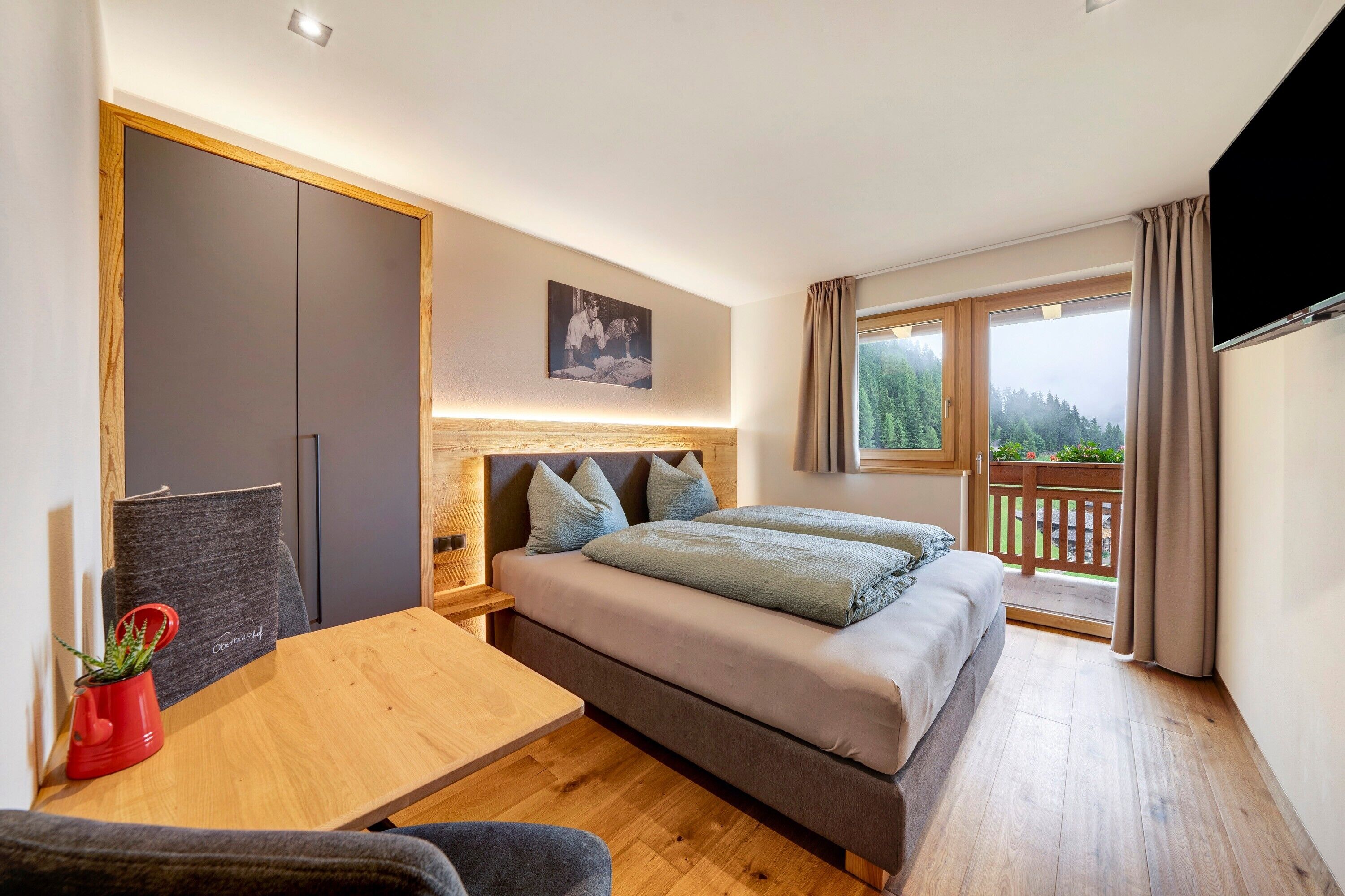 Une chambre avec un lit, un bureau, une chaise, une télévision et un balcon avec vue.