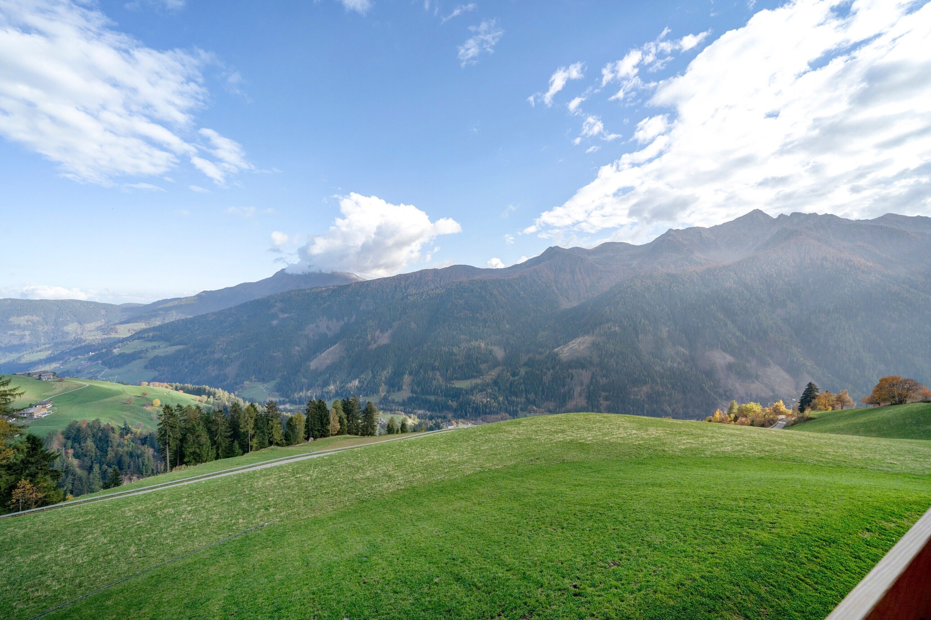 Een panoramisch uitzicht op een bergachtig landschap met een heldere lucht en een groen veld op de voorgrond.