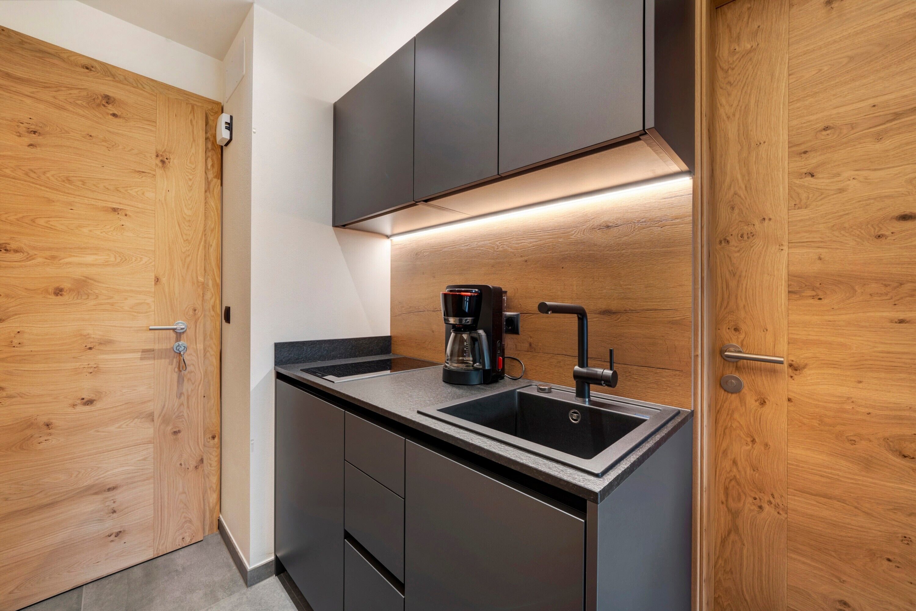 A modern kitchen with a built-in sink, dark cabinetry, and a coffee maker.