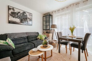 Una sala de estar con un sofá oscuro, una mesa de comedor con sillas, una lámpara y un aparador.