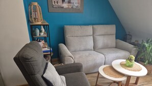 A living room with a grey sofa, a dark armchair, and a small round table with a decorative item. - Apartment Between Land and Sea – Peaceful Retreat Near Saint-Malo & Mont-Saint-Michel (Baguer-Pican)