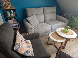 En hyggelig stue med en grå sofa, en stuestol med et mønster og et rundt bord med en grøn vase.