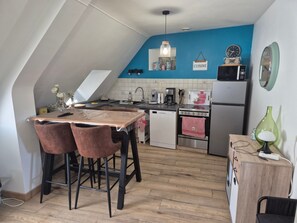 Une cuisine compacte avec un coin repas, un mur d’accent bleu et un petit réfrigérateur.