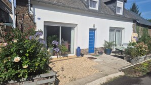 A two-story house with a garage, a blue door, and a garden with various plants and flowers.