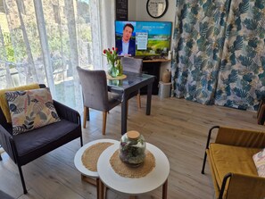 Una sala de estar con un sofá, dos mesas redondas, un televisor y un ventanal con cortinas.