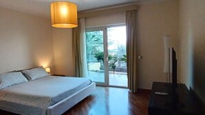 Een slaapkamer met een bed, een televisie, een lamp en een schuifdeur naar een buitenruimte.