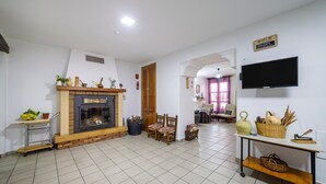 Una sala de estar con chimenea, un televisor montado en la pared y un comedor visible a través de un arco.